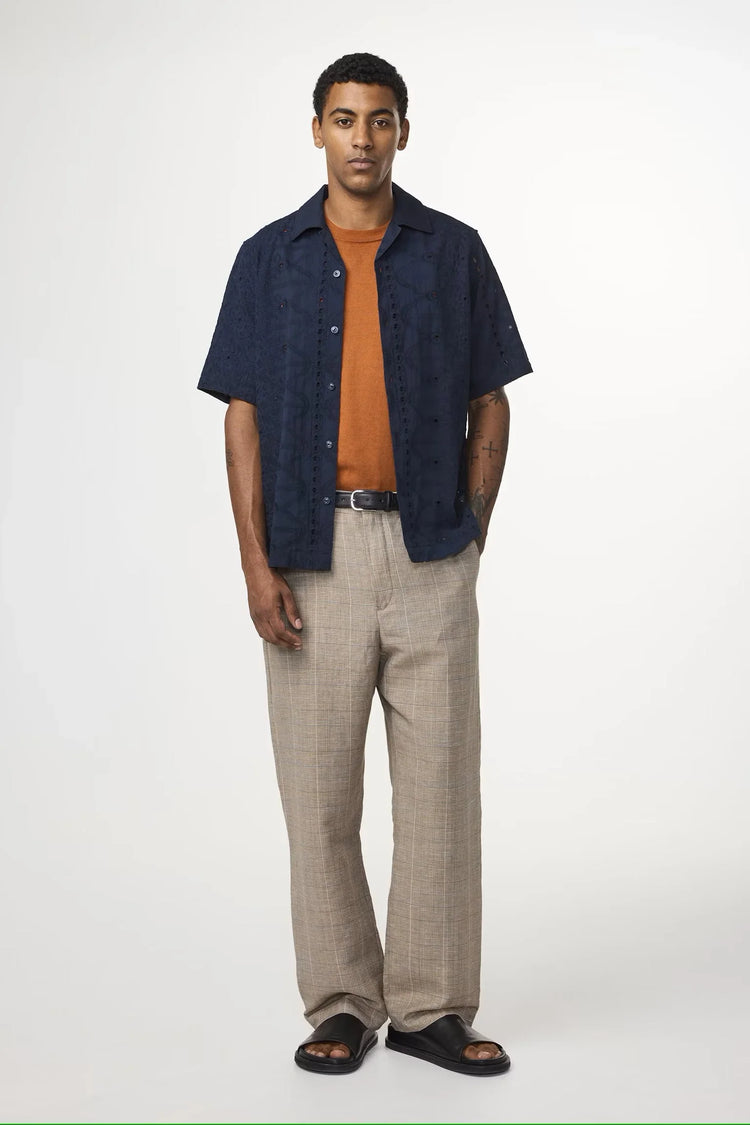 Man i modern herrklädsel med marinblå skjorta, orange t-shirt, beige kostymbyxor och sandaler.