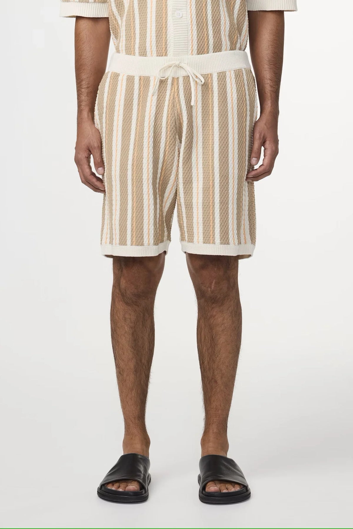Herr i beige och vita randiga shorts med dragsko och svarta sandaler, sommarkläder