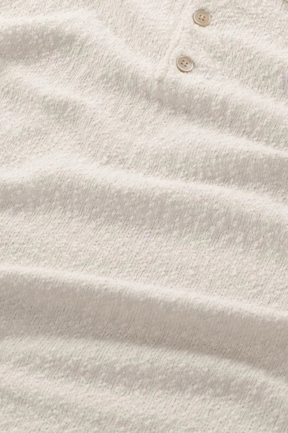 Närbild på beige herrtröja i texturerat tyg med två knappar, klassiskt herrmode.