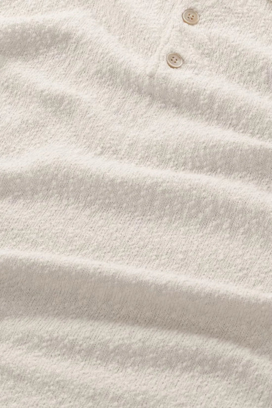 Närbild på beige herrtröja i texturerat tyg med två knappar, klassiskt herrmode.