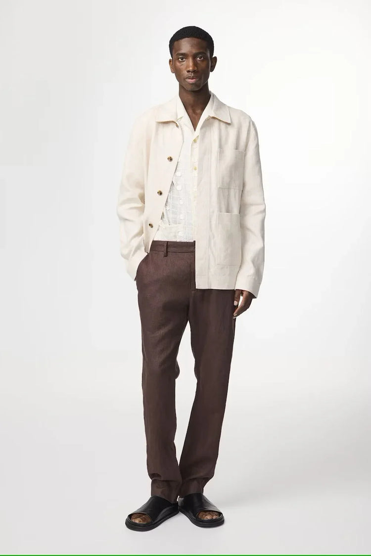 Man i beige linnejacka, vit skjorta och bruna byxor, modernt herrmode.