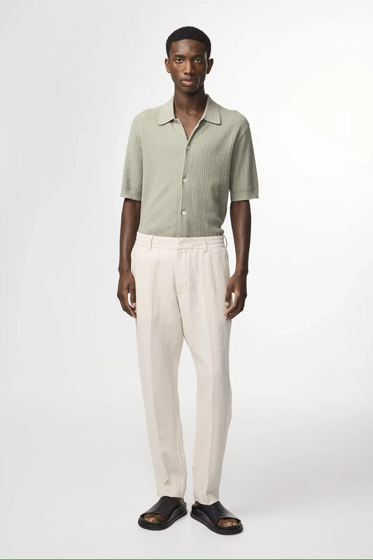 Man i ljusgrön stickad skjorta, beige linnebyxor och svarta sandaler mot vit bakgrund