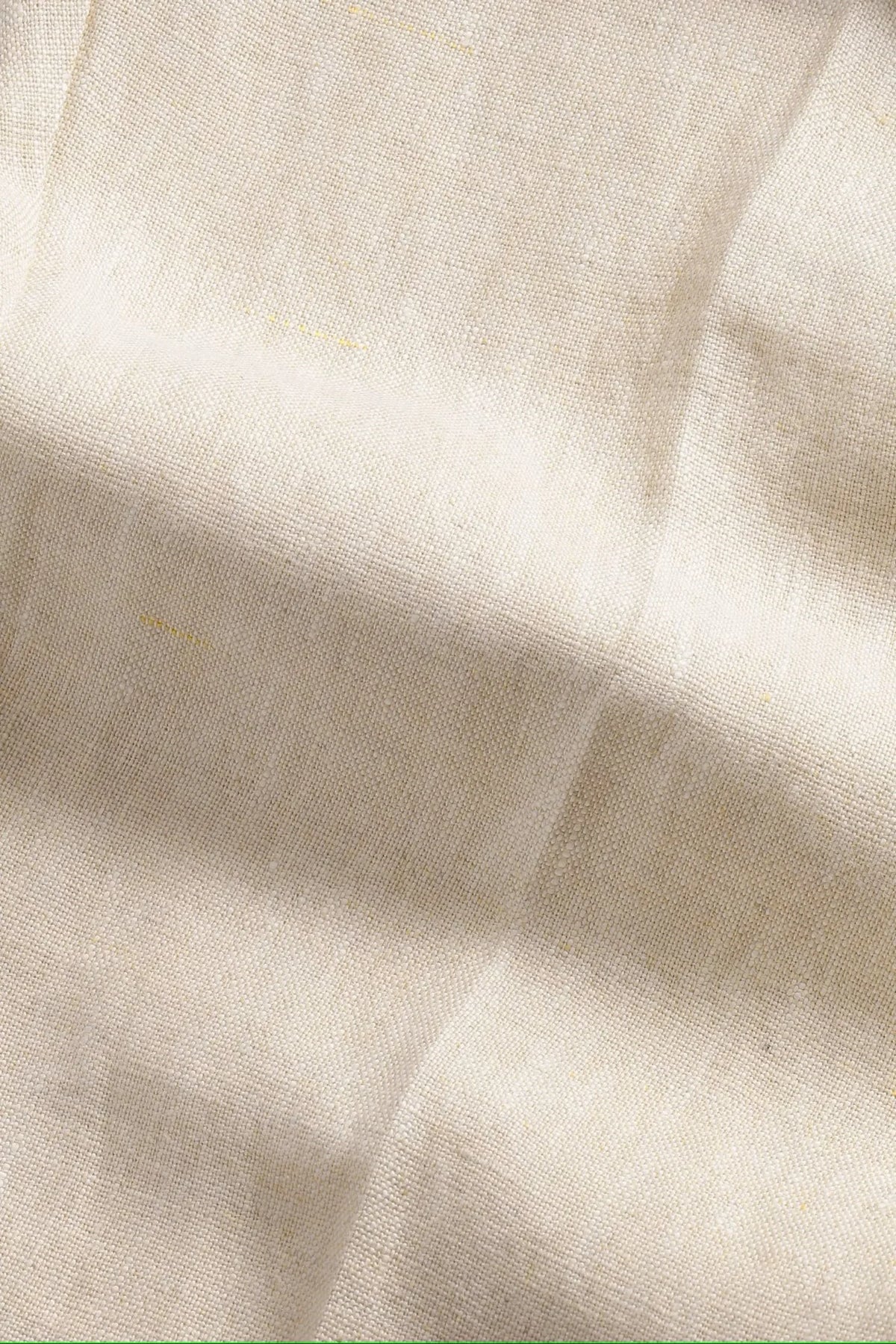 Närbild på naturfärgat linnetyg med synlig vävstruktur och veck, herrmode textil