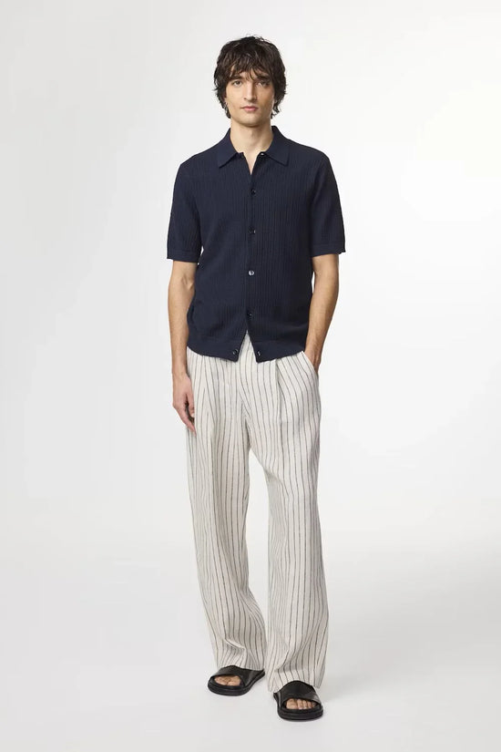 Man i mörkblå skjorta med kort ärm och beige randiga byxor, herrmode, sommarstil