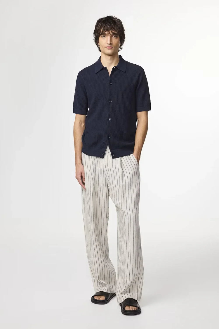 Man i mörkblå skjorta med kort ärm och beige randiga byxor, herrmode, sommarstil