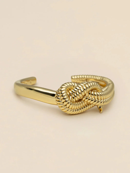 Elegant herrarmband i guld med dekorativ knut, klassisk accessoar på beige bakgrund