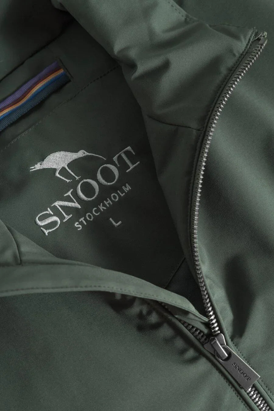 Närbild på grön herrjacka med dragkedja och broderad logotyp från Snoot Stockholm