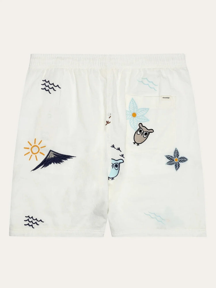 Vita herrshorts med broderade motiv av ugglor, blommor, vågor och solen, elastisk midja
