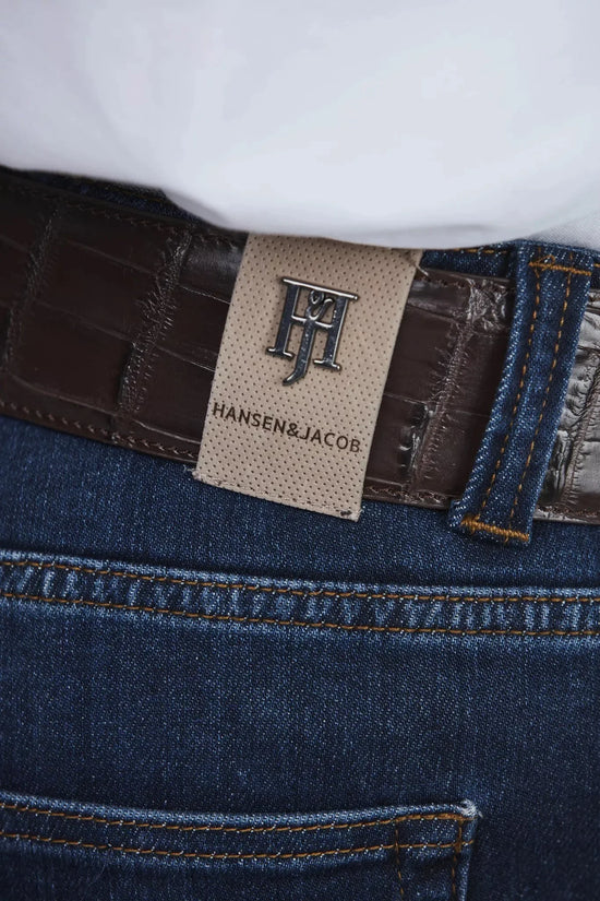 Närbild av blå denimbyxa med brun läderbälte och detaljrik sömnad.