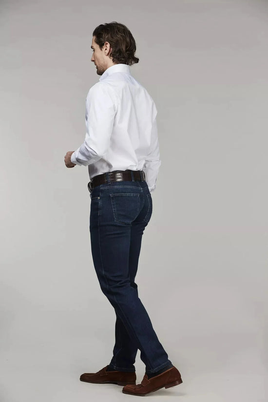 Man i vit skjorta och mörkblå denimbyxor, sett bakifrån, mot ljus bakgrund.