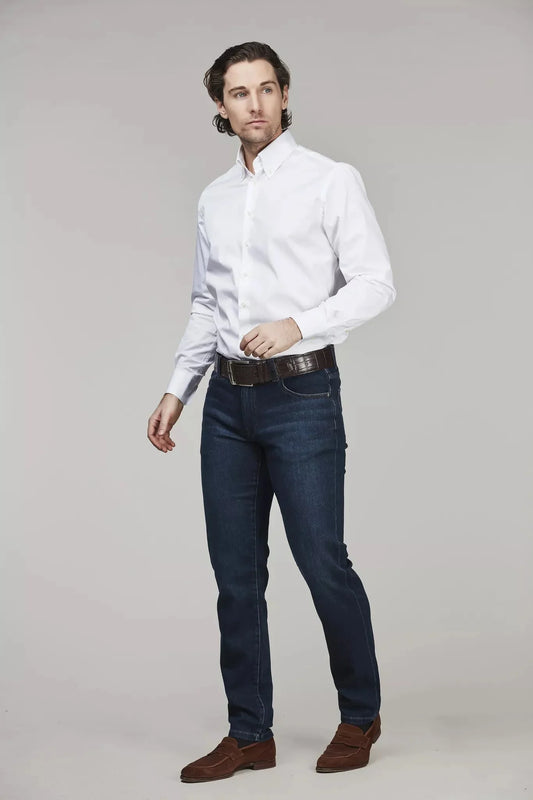 Man i vit skjorta och mörkblå jeans, klassiskt herrmode mot ljus bakgrund.