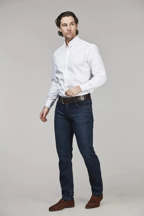 Man i vit skjorta och mörkblå jeans, klassiskt herrmode mot ljus bakgrund.
