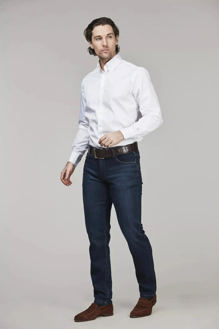 Man i vit skjorta och mörkblå jeans, klassiskt herrmode mot ljus bakgrund.