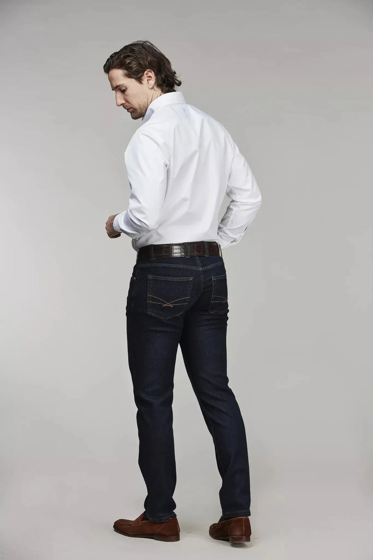 Herr i vit skjorta och mörkblå denimbyxor, bakifrån, mot ljus bakgrund