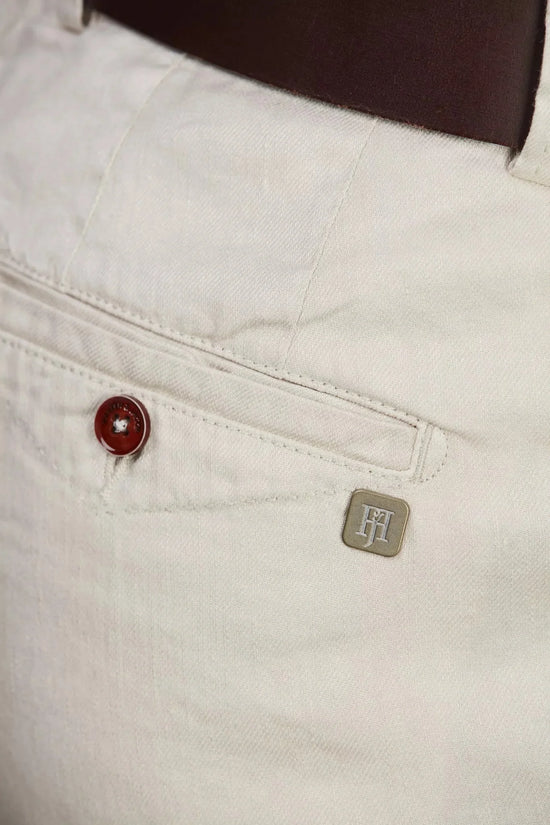 Detaljbild på bakficka av vita bomull-lin chinos för herr, knapp och metallmärke synliga.