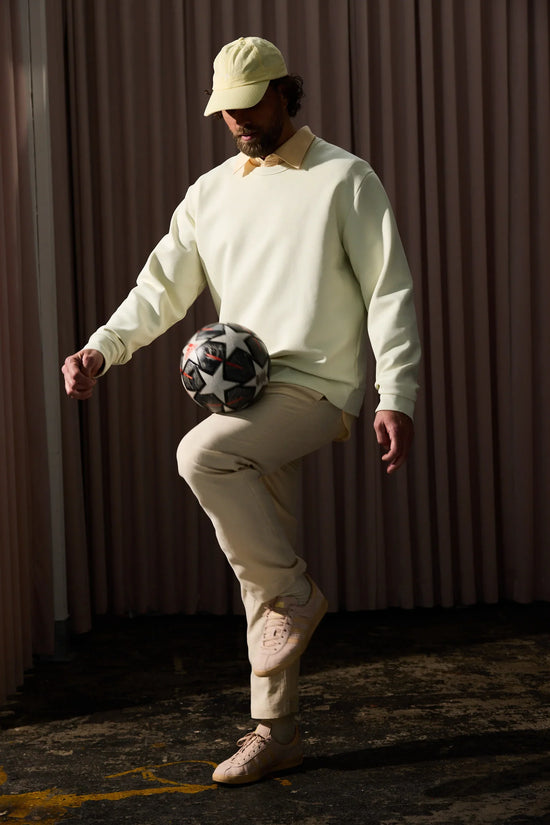 Ljusgul sweatshirt herr, beigefärgade byxor, beige keps, sneakers