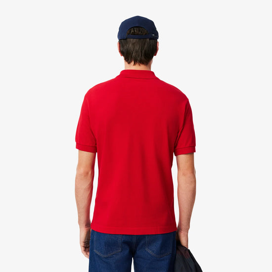 Man i röd pikétröja, blå jeans och marinblå keps, sedd bakifrån mot vit bakgrund.