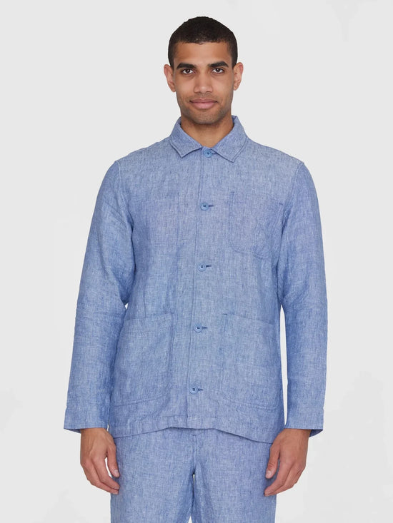 Man i blå linneskjorta, overshirt med knappar och fickor, mot vit bakgrund.