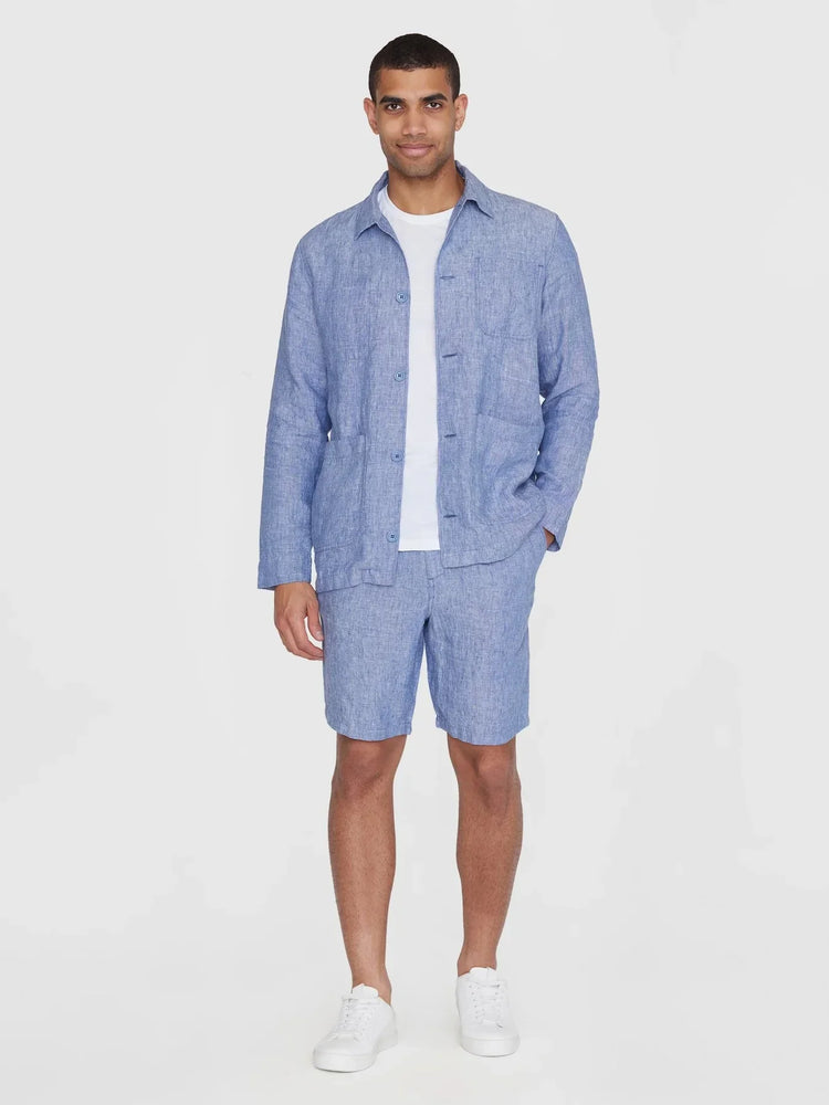 Man i blå linneskjorta och matchande shorts, vit t-shirt och vita sneakers