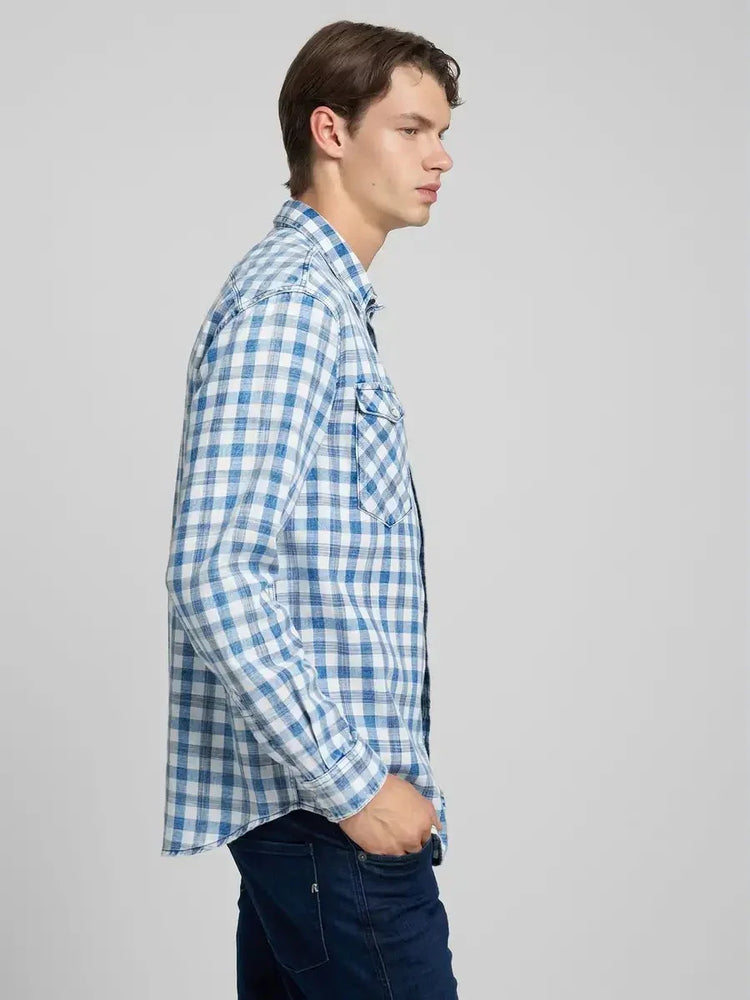 Man i blåvitrutig skjorta och mörka jeans, mode för herr, sidovy mot ljus bakgrund