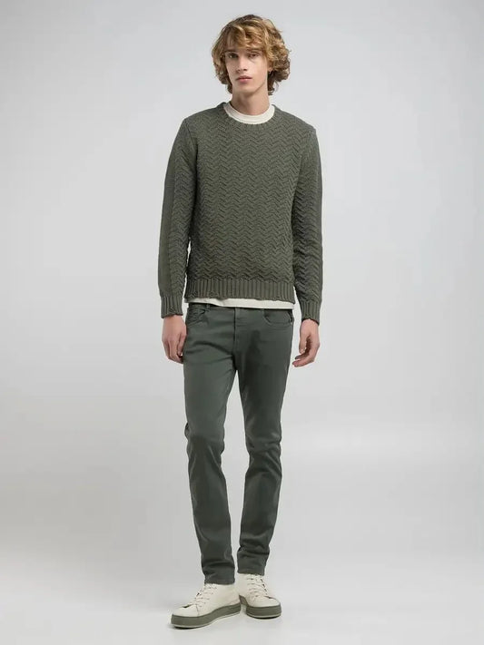 Man i gröna smala byxor, stickad tröja och vita sneakers mot ljus bakgrund