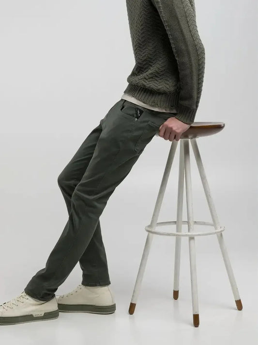 Man i gröna byxor och stickad tröja sitter på pall, stilren herrmode outfit