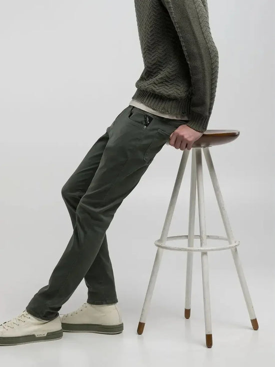 Man i gröna byxor och stickad tröja sitter på pall, stilren herrmode outfit