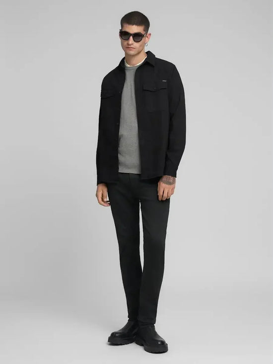 Man i svarta jeans, grå tröja och svart skjortjacka, moderna herrkläder, helkroppsbild.