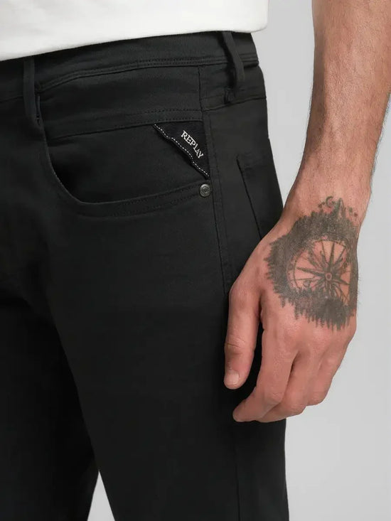 Svarta jeans för herr, närbild på ficka med Replay-logotyp och tatuering på handen