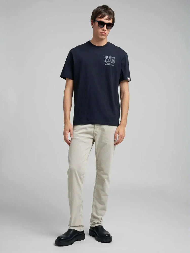 Man i mörkblå t-shirt, ljusa jeans och svarta boots mot ljus bakgrund