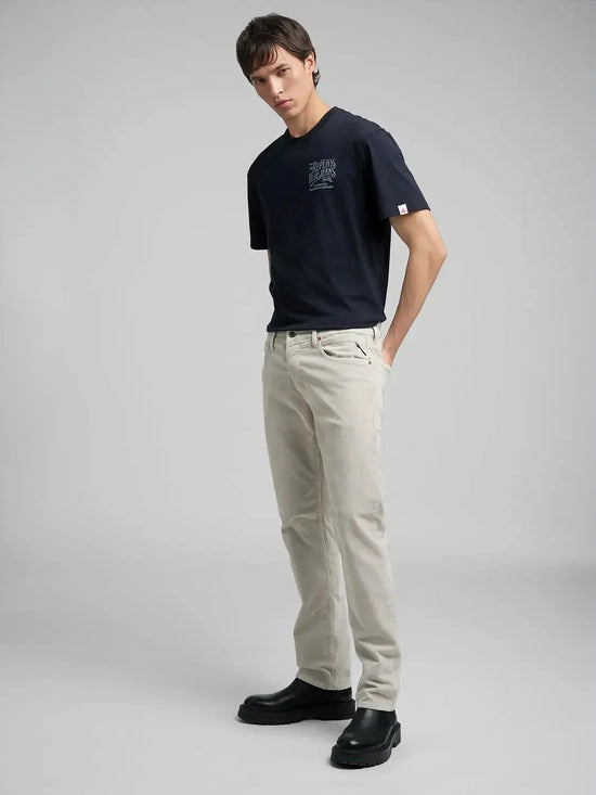Ung man i svart t-shirt, ljusa chinos och svarta boots mot grå bakgrund