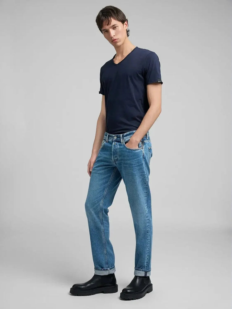Man i mörkblå t-shirt, blå jeans och svarta boots mot ljus bakgrund