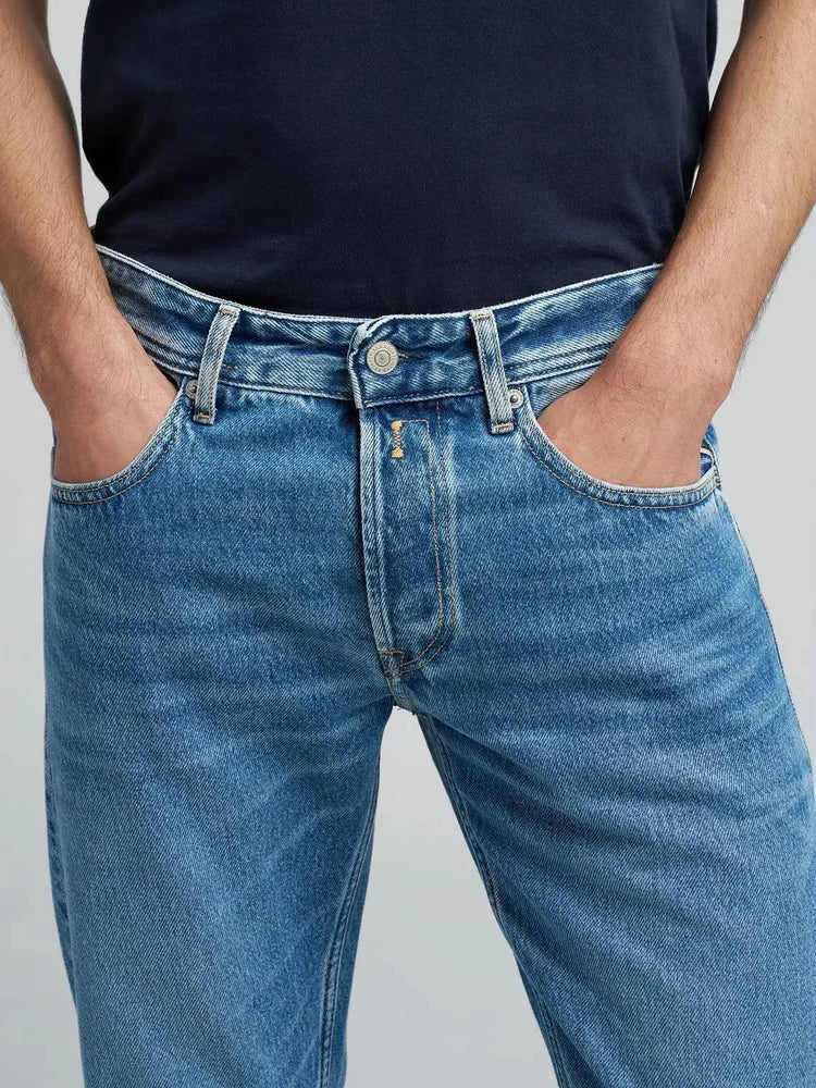 Herr i blå jeans och mörk t-shirt, klassiskt snitt, händer i fickorna.