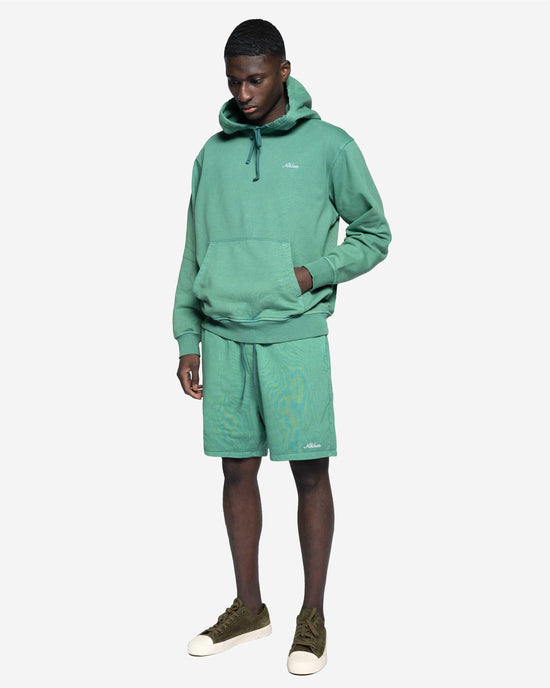 Man i grön hoodie och matchande shorts, avslappnad herrklädstil, vit bakgrund