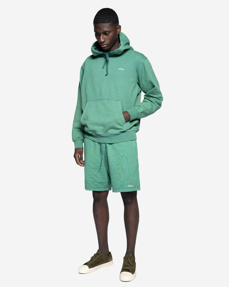Man i grön hoodie och matchande shorts, avslappnad herrklädstil, vit bakgrund