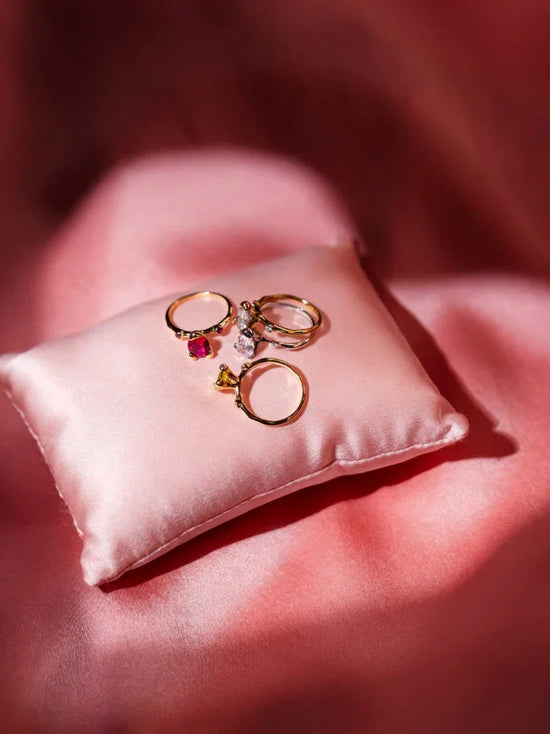 Guldringar med stenar på rosa sidenkudde, elegant smyckesarrangemang