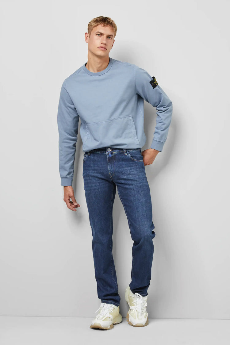 Man i ljusblå sweatshirt och raka blå jeans, casual herrmode, mot vit bakgrund