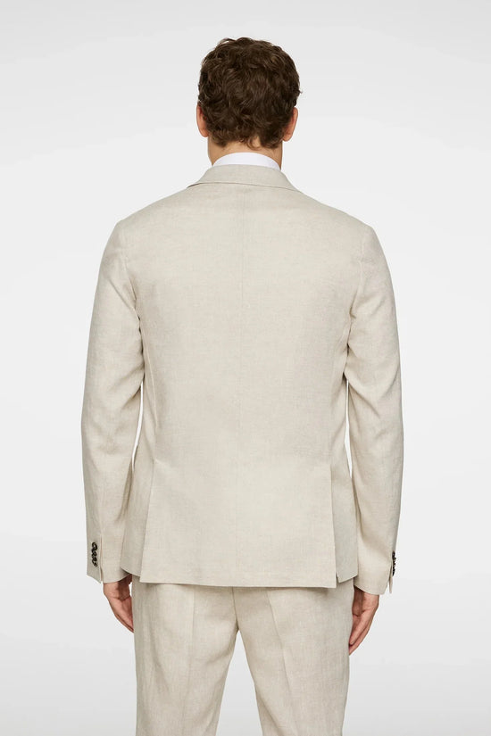 Man i beige linnekostym, bakifrån, med vit skjorta mot ljus bakgrund