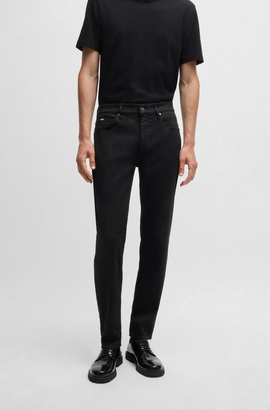 Man i svarta jeans, svart t-shirt och svarta skor mot ljus bakgrund, klassisk herrstil