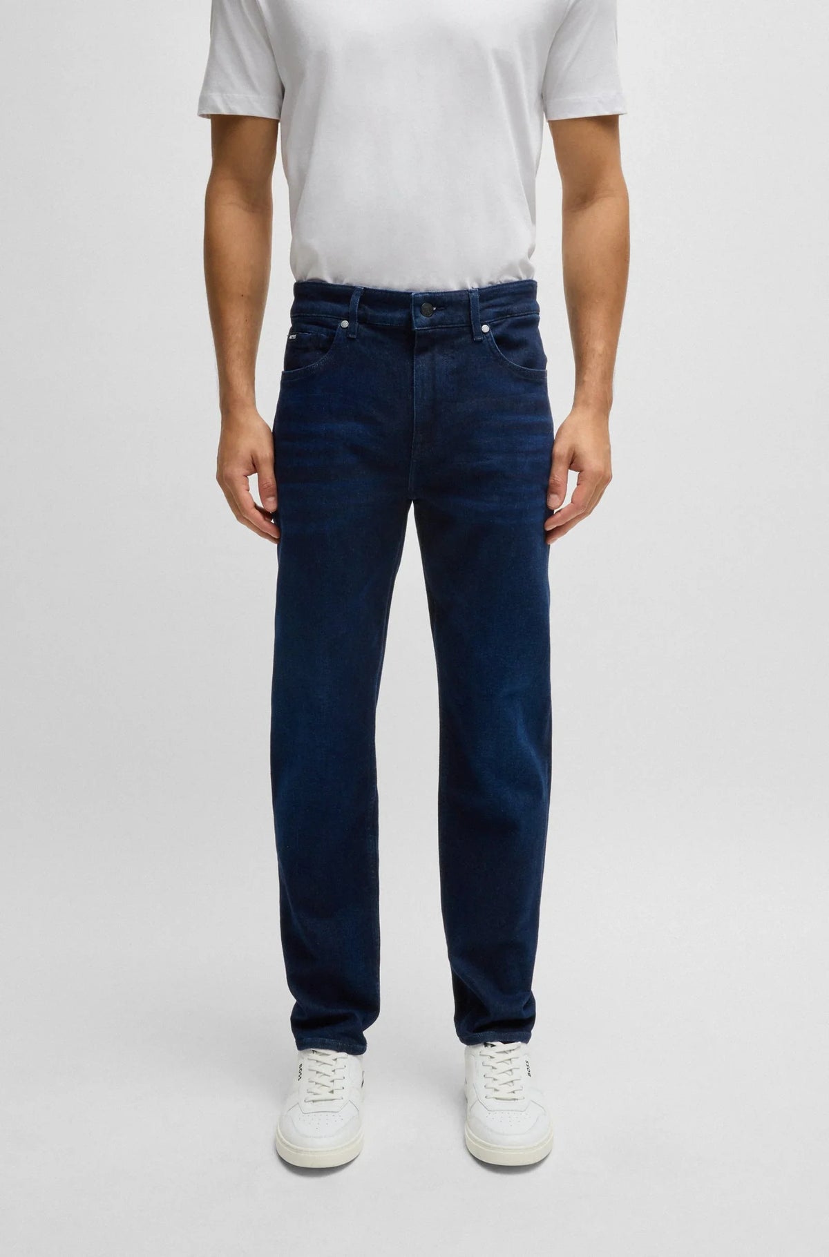 Man i mörkblå raka jeans och vit t-shirt, casual herrkläder mot ljus bakgrund