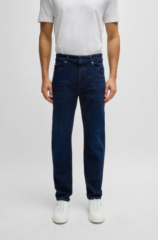 Man i mörkblå raka jeans och vit t-shirt, casual herrkläder mot ljus bakgrund