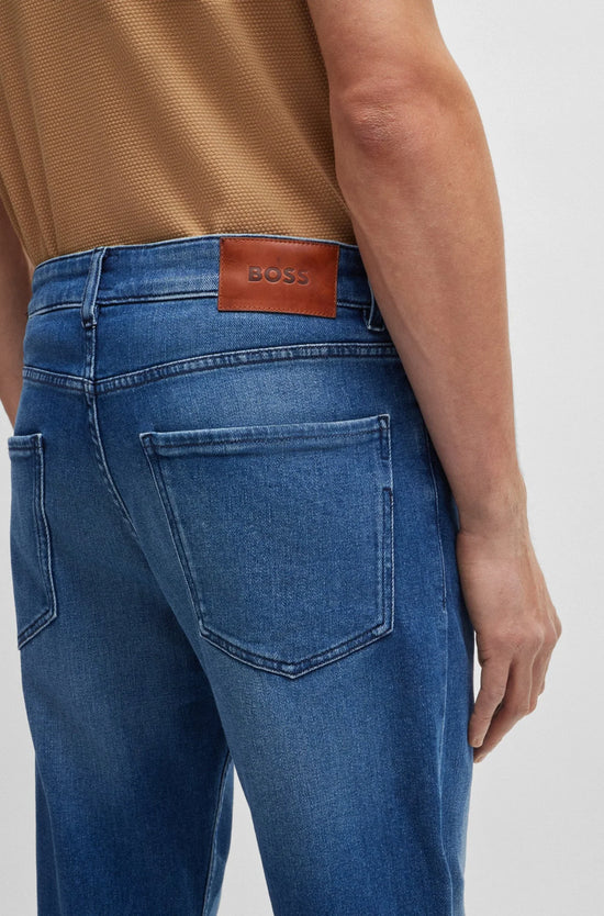 Närbild av herrjeans med blå denim och bakficka, läderpatch med BOSS-logga