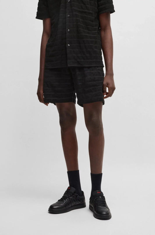 Man i svarta herrshorts och skjorta med textur, svarta strumpor och sneakers