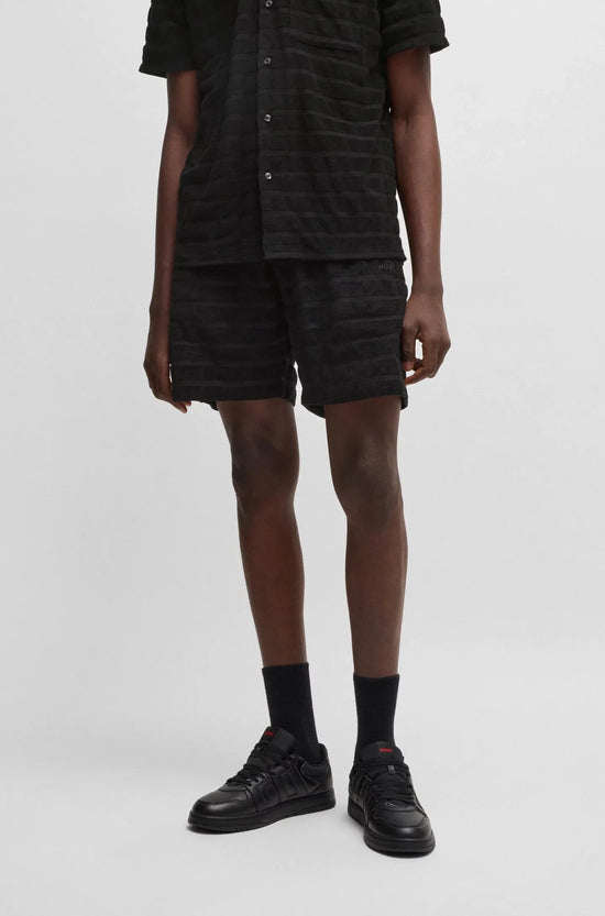 Man i svarta herrshorts och skjorta med textur, svarta strumpor och sneakers
