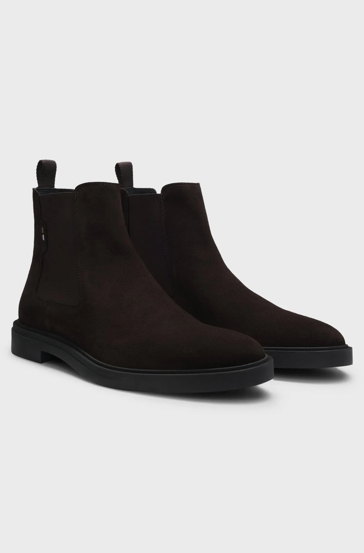 Mörkbruna Chelsea boots i mocka för herr, klassisk modell med svart sula på vit bakgrund.