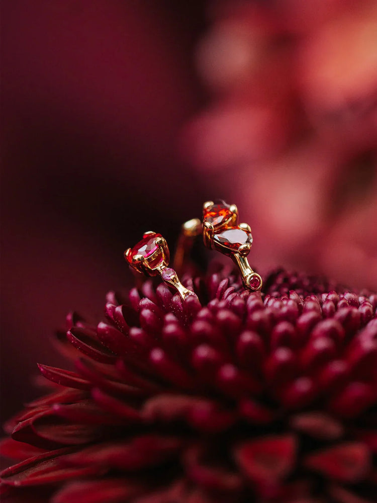 Guldörhängen med röda stenar på en mörkröd blomma, elegant accessoar för herrmode.