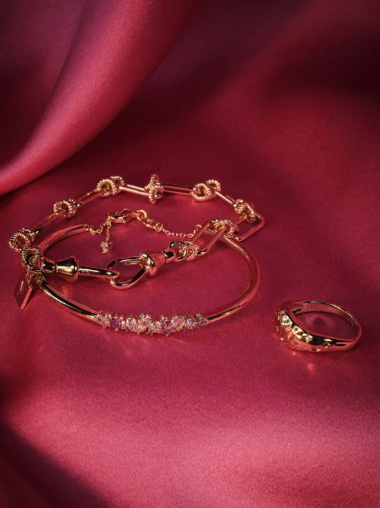 Guldsmycken, armband och ring med kristaller på rosa satinbakgrund