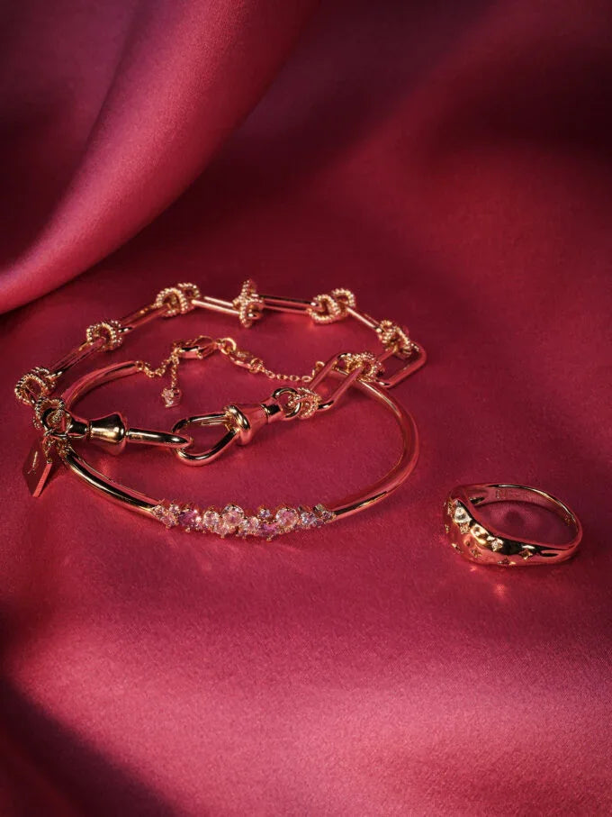 Guldsmycken, armband och ring med kristaller på rosa satinbakgrund