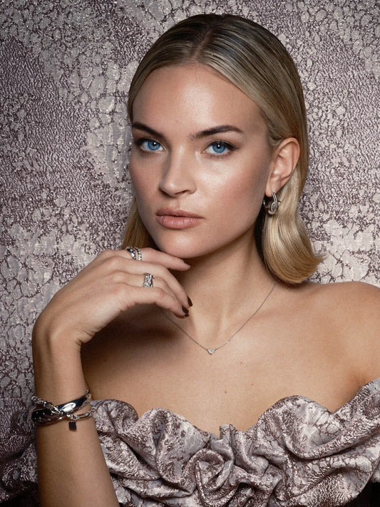 Kvinna med blondt hår, eleganta silversmycken och mönstrad klänning mot mönstrad bakgrund