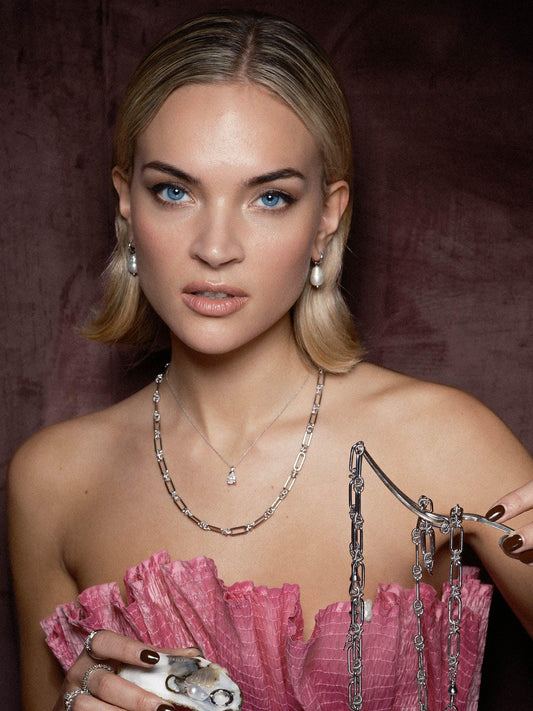 Kvinna med kort blont hår bär silverhalsband och örhängen samt rosa klänning